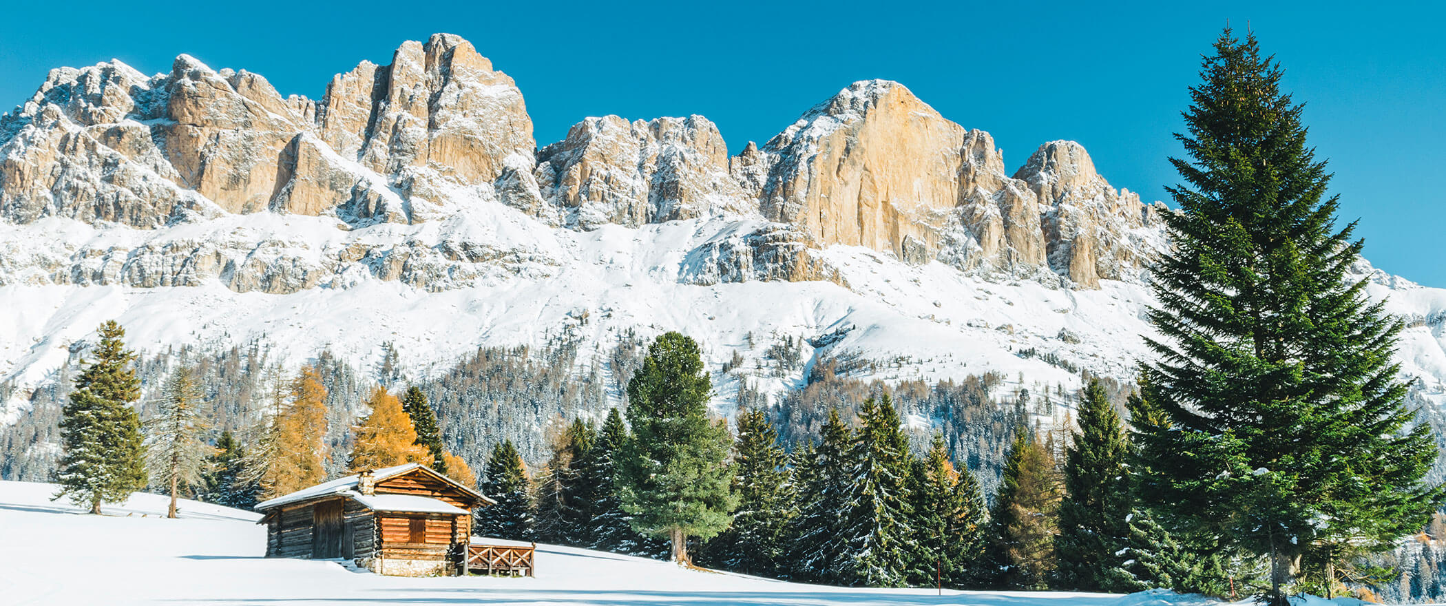 Capanna in legno in mezzo a un campo innevato, con alle spalle suggestive cime di montagna - Vitalhotel Erica