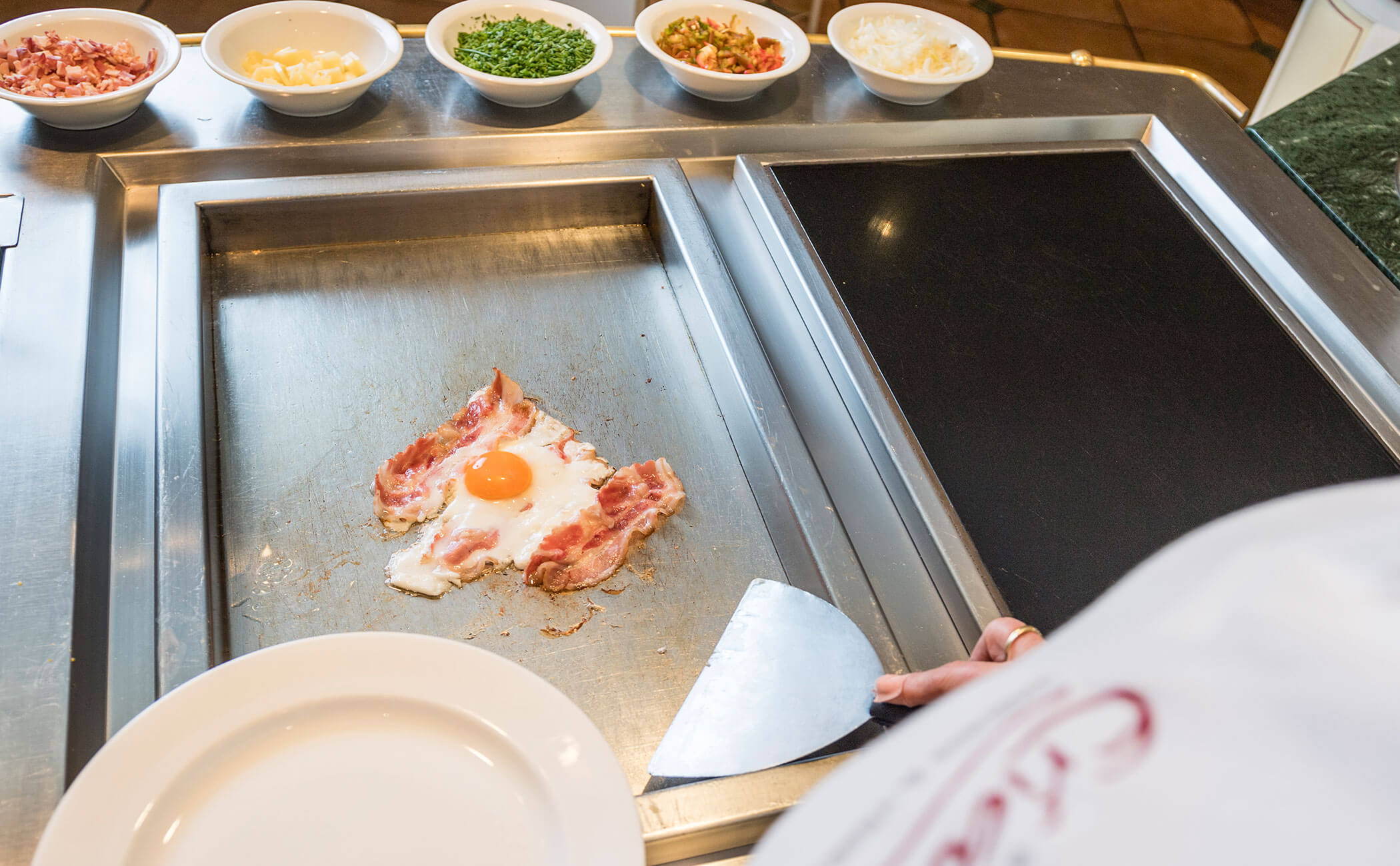 Lo chef della colazione cucina l'uovo fritto con pancetta - Vitalhotel Erica