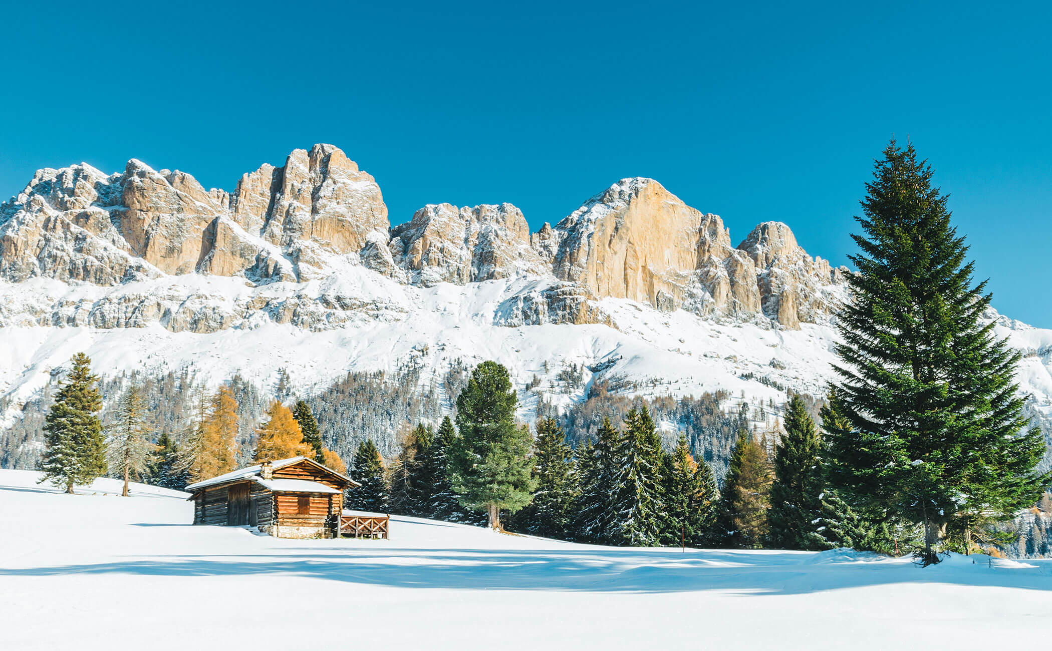 Baita in legno in mezzo a un campo innevato, con alle spalle le suggestive cime delle montagne - Vitalhotel Erica