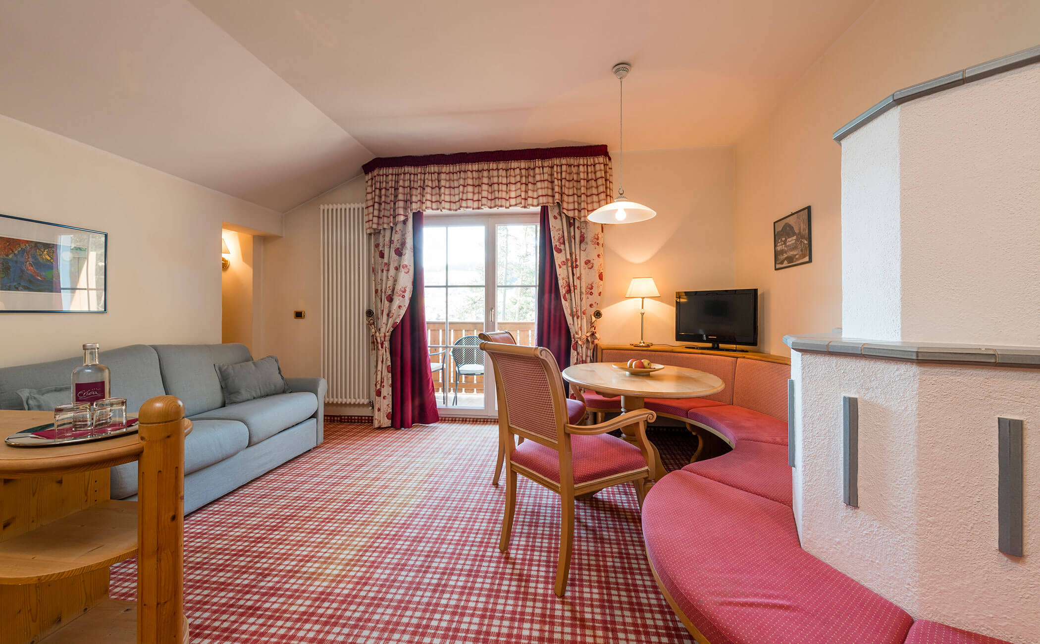 Divano azzurro e panca d'angolo rossa accanto alla stufa a legna nell'appartamento familiare - Vitalhotel Erica