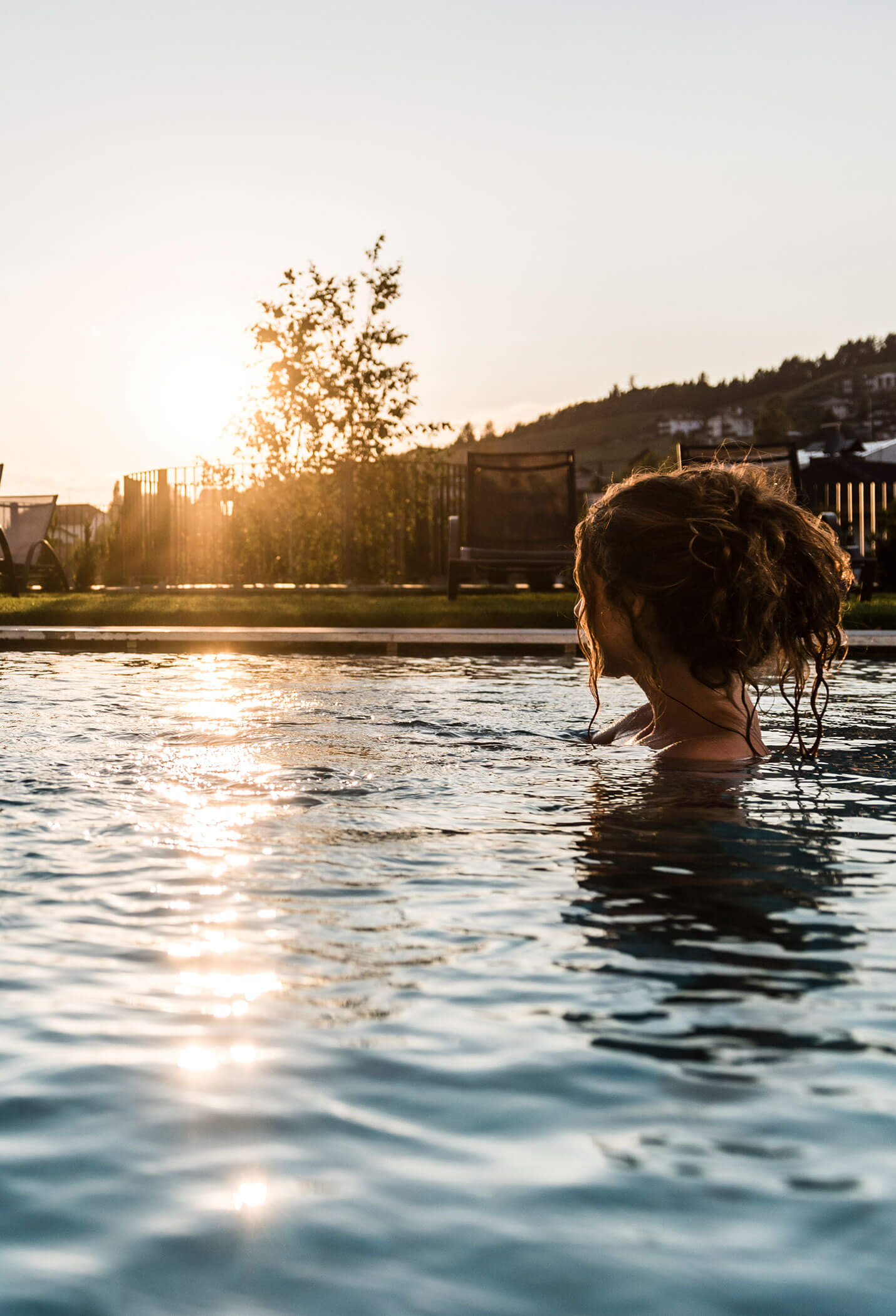 Una donna nella piscina all'aperto mentre il sole tramonta - Vitalhotel Erica