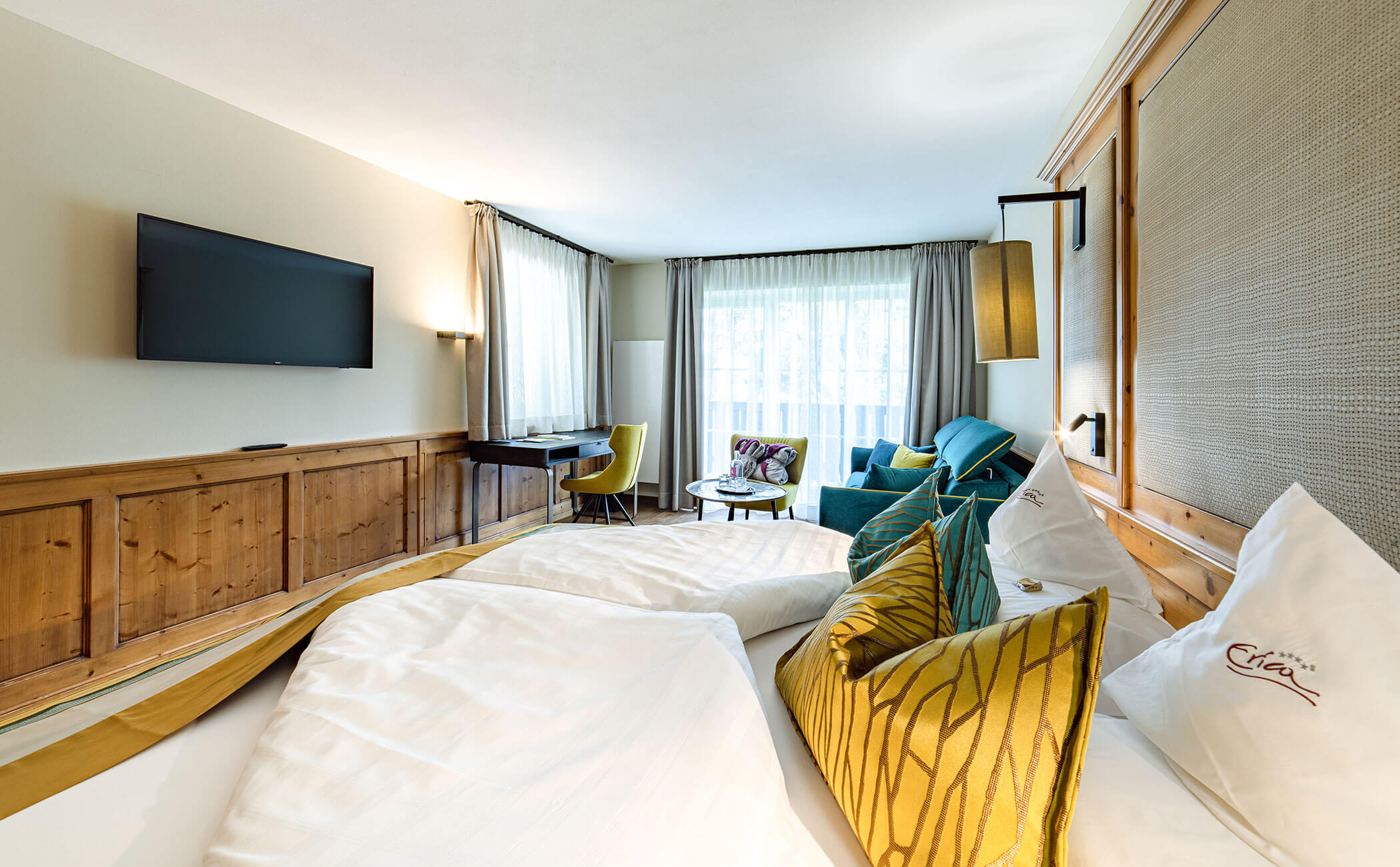 Letto matrimoniale e zona giorno con tende verdi nella camera Latemar Superior - Vitalhotel Erica