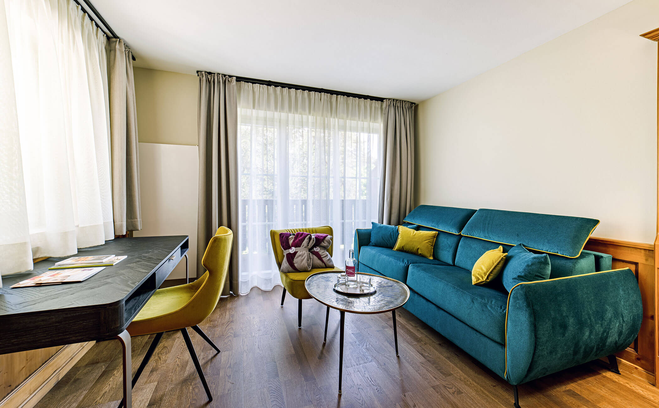 Divano blu con cuscini verdi e scrivania con sedia verde nella camera Latemar Superior - Vitalhotel Erica