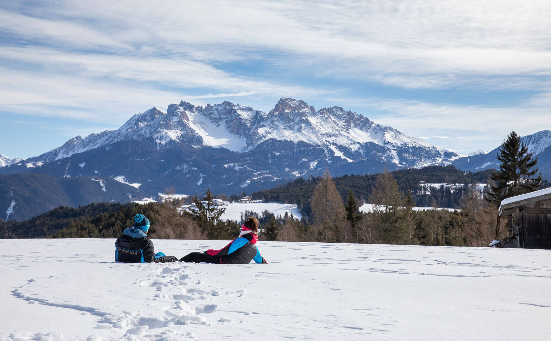 Una coppia seduta sulla neve a guardare il paesaggio montano innevato - Vitalhotel Erica