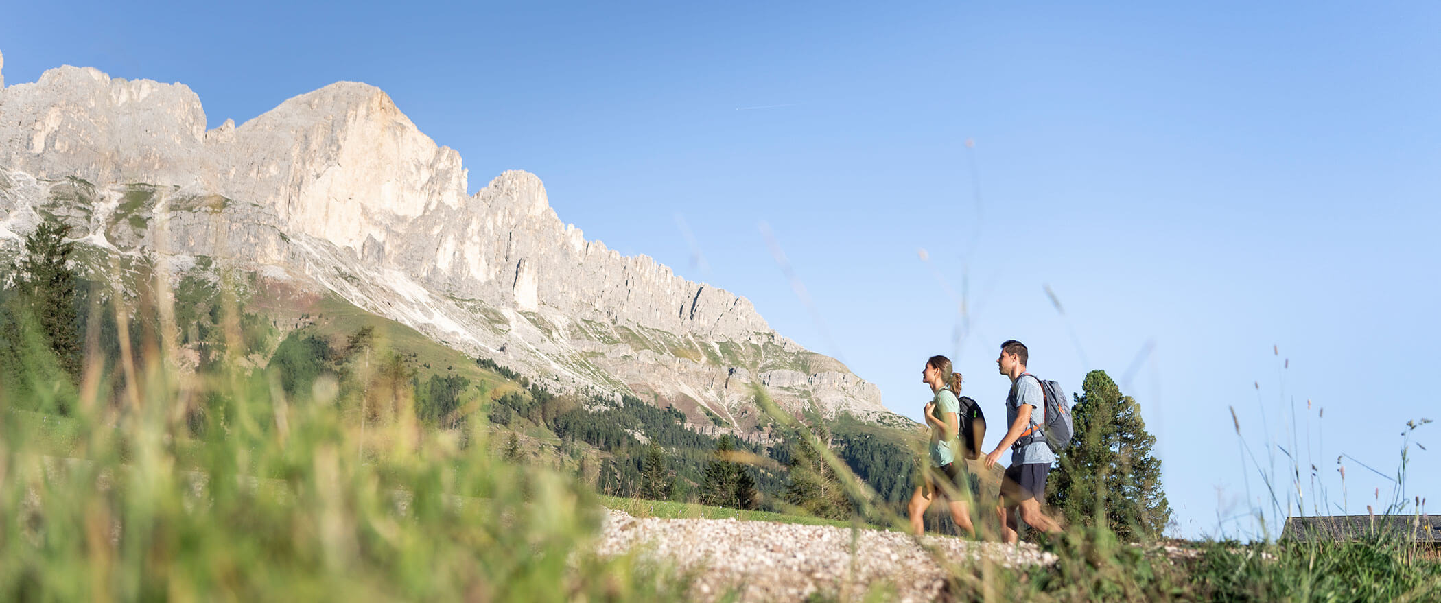 Una donna e un uomo su un sentiero di ghiaia nelle Dolomiti, con le cime alle spalle - Vitalhotel Erica