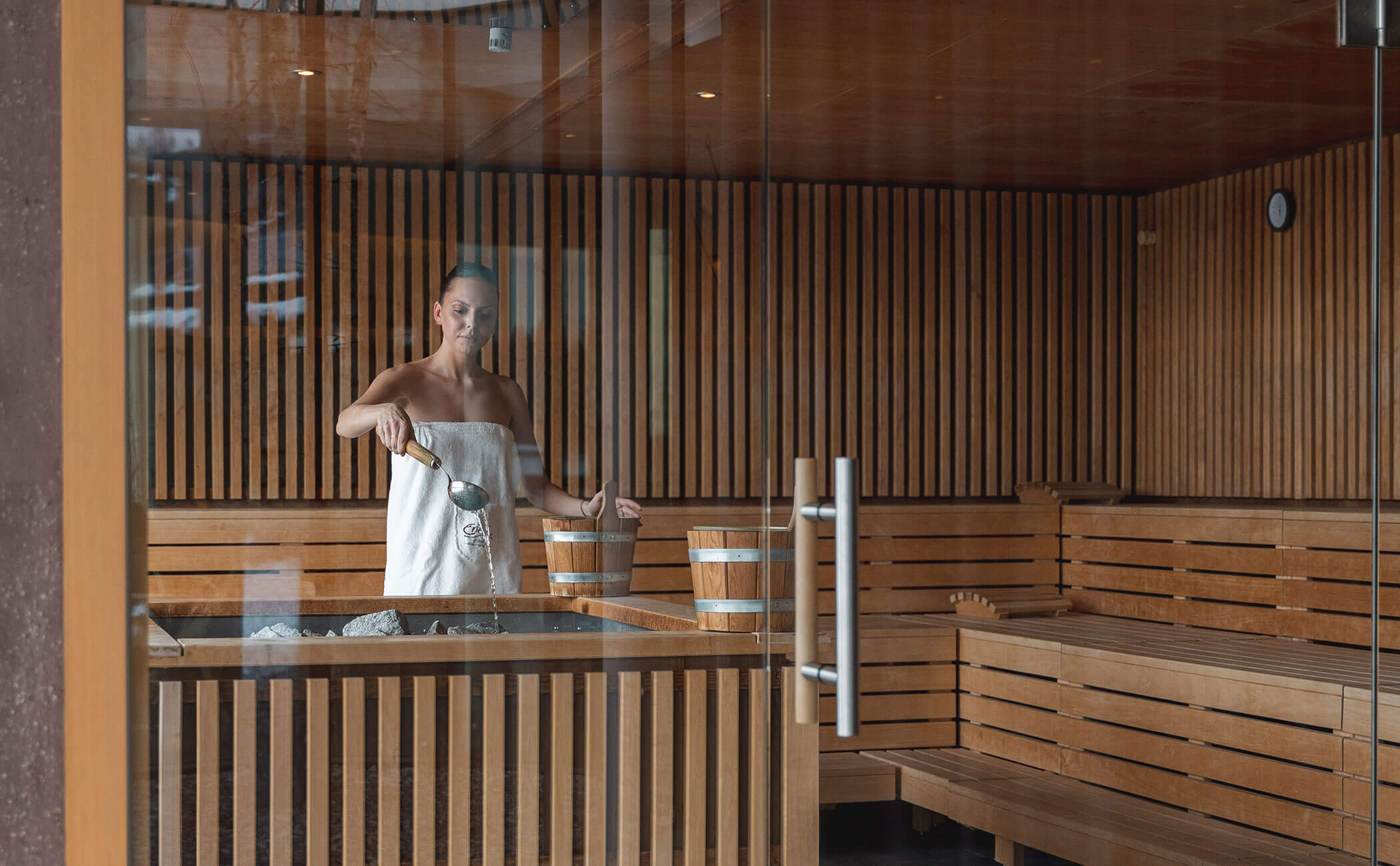 Una donna versa acqua sulle pietre calde della sauna a infusione - Vitalhotel Erica