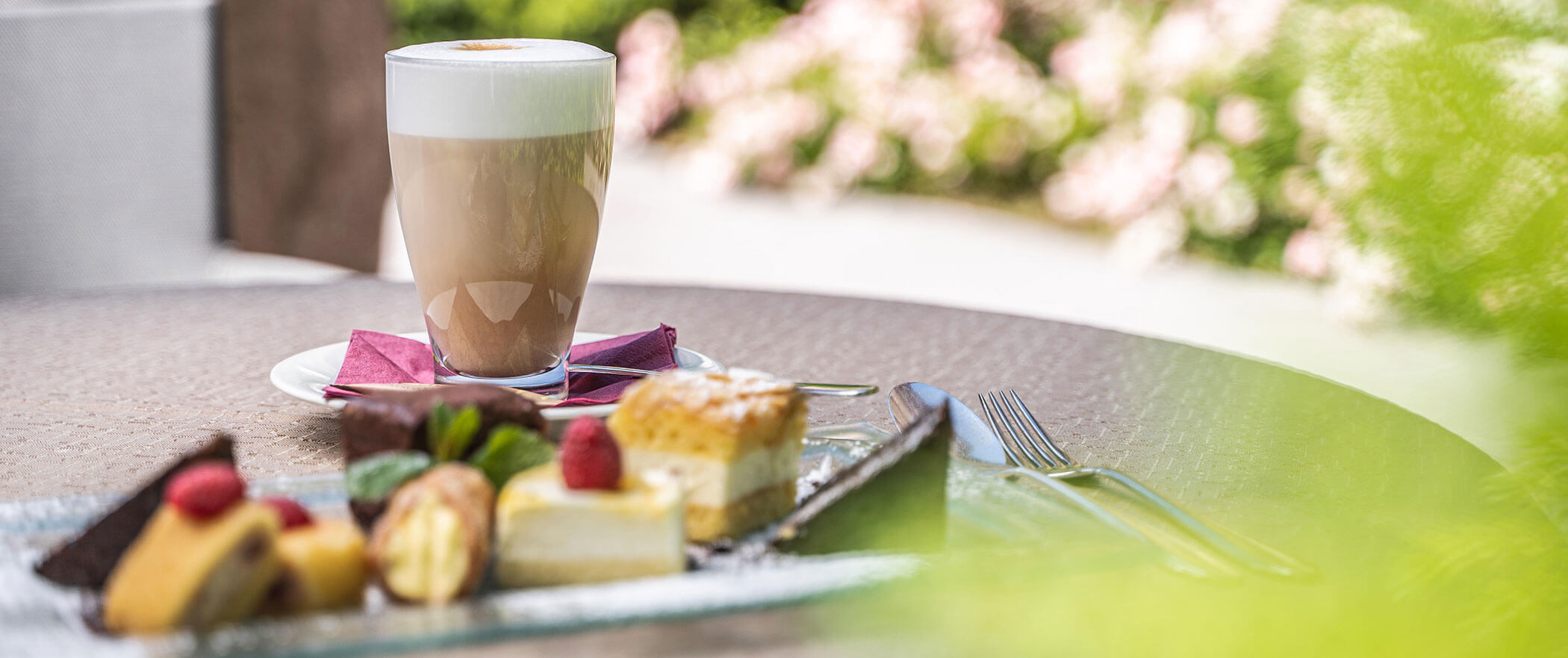 Vari pezzi di torta e un latte macchiato su un tavolo in terrazza - Vitalhotel Erica