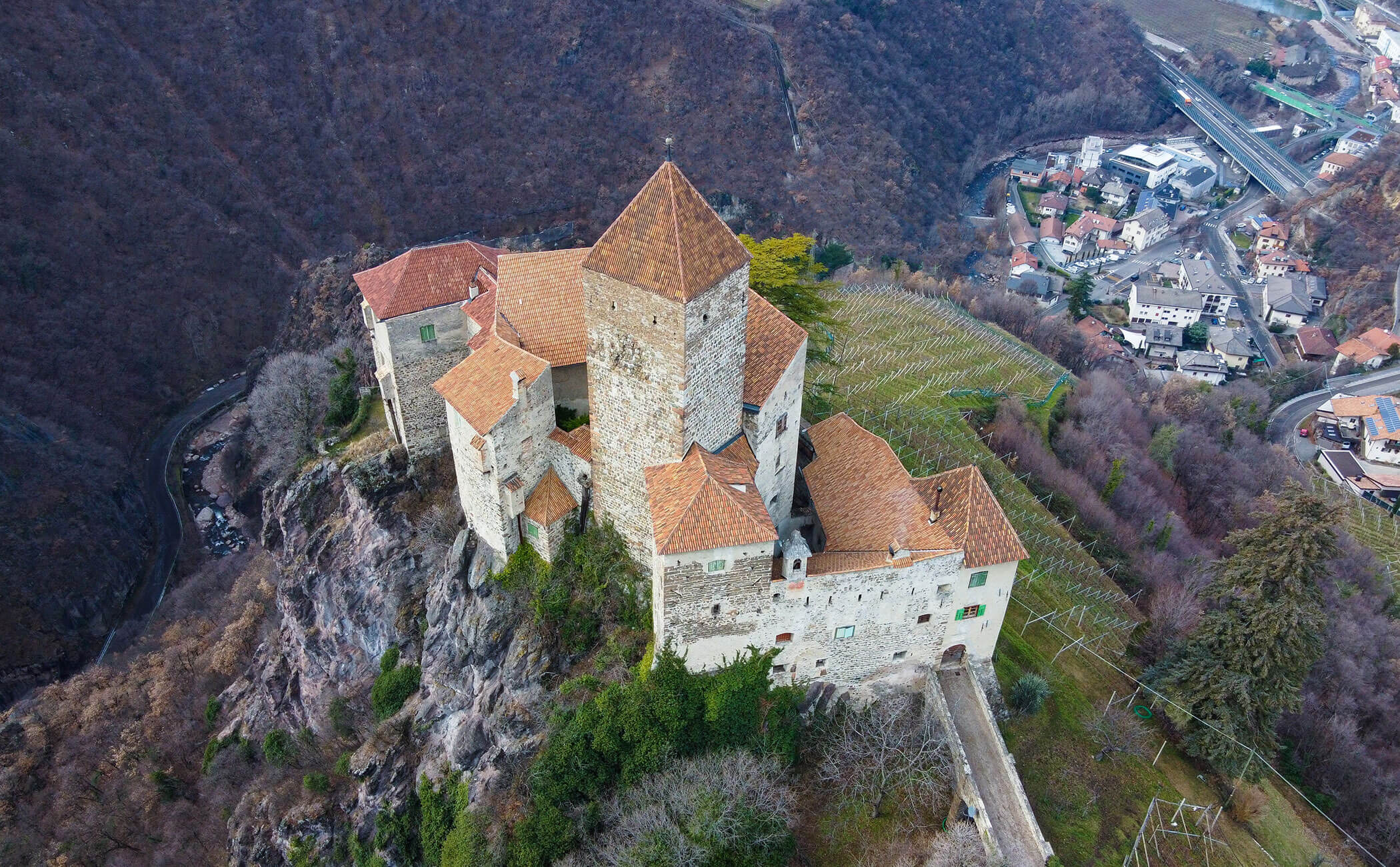 Ripresa da drone di un castello su una montagna, con diverse case a valle - Vitalhotel Erica