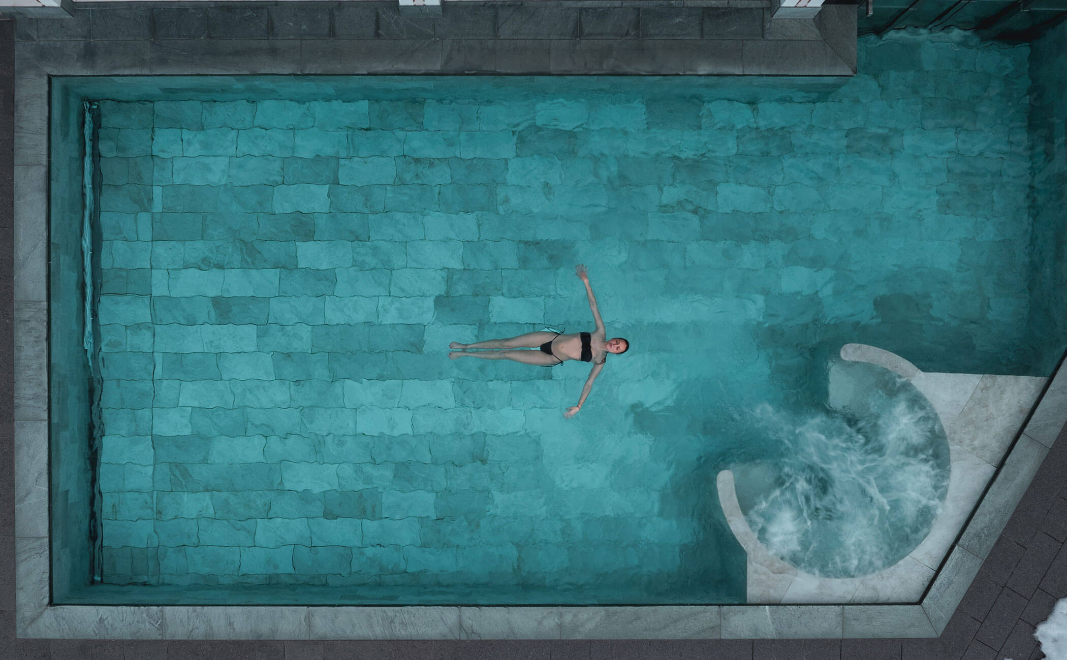 Vista dall'alto di una donna che galleggia nell'acqua della piscina esterna - Vitalhotel Erica