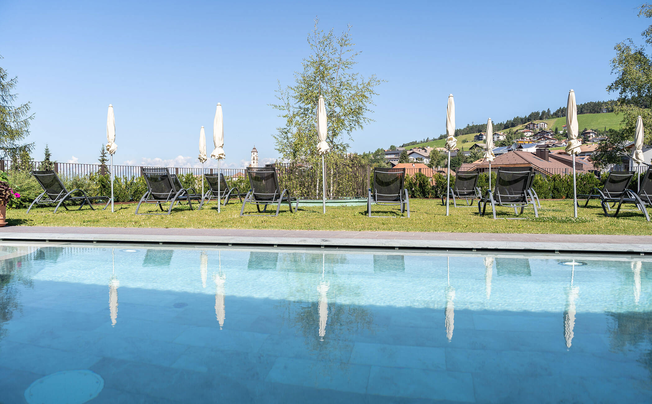 Vista dalla piscina esterna al prato con diverse sedie a sdraio e ombrelloni - Vitalhotel Erica