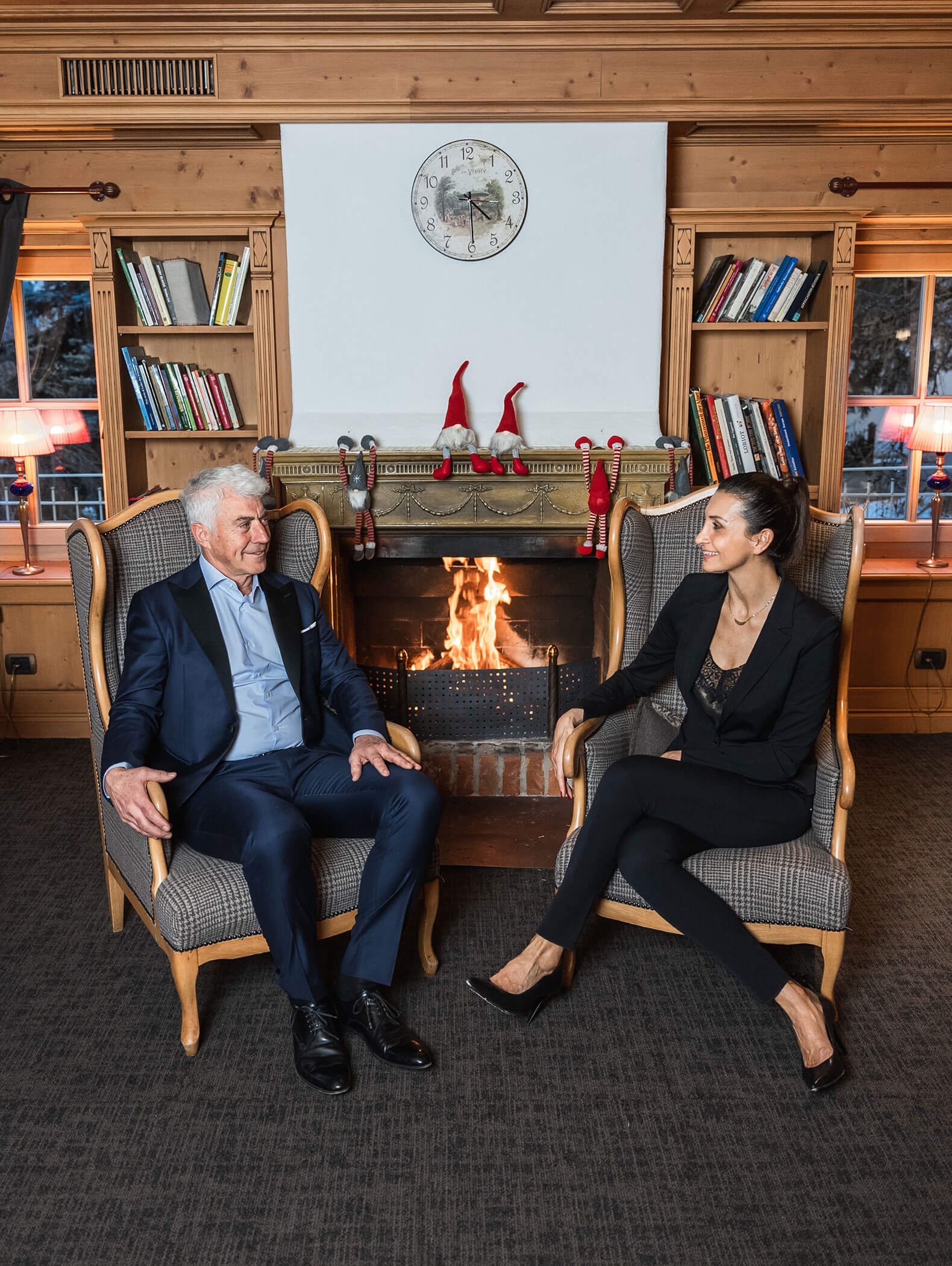 I padroni di casa sono seduti su una poltrona, con il fuoco a legna alle spalle - Vitalhotel Erica