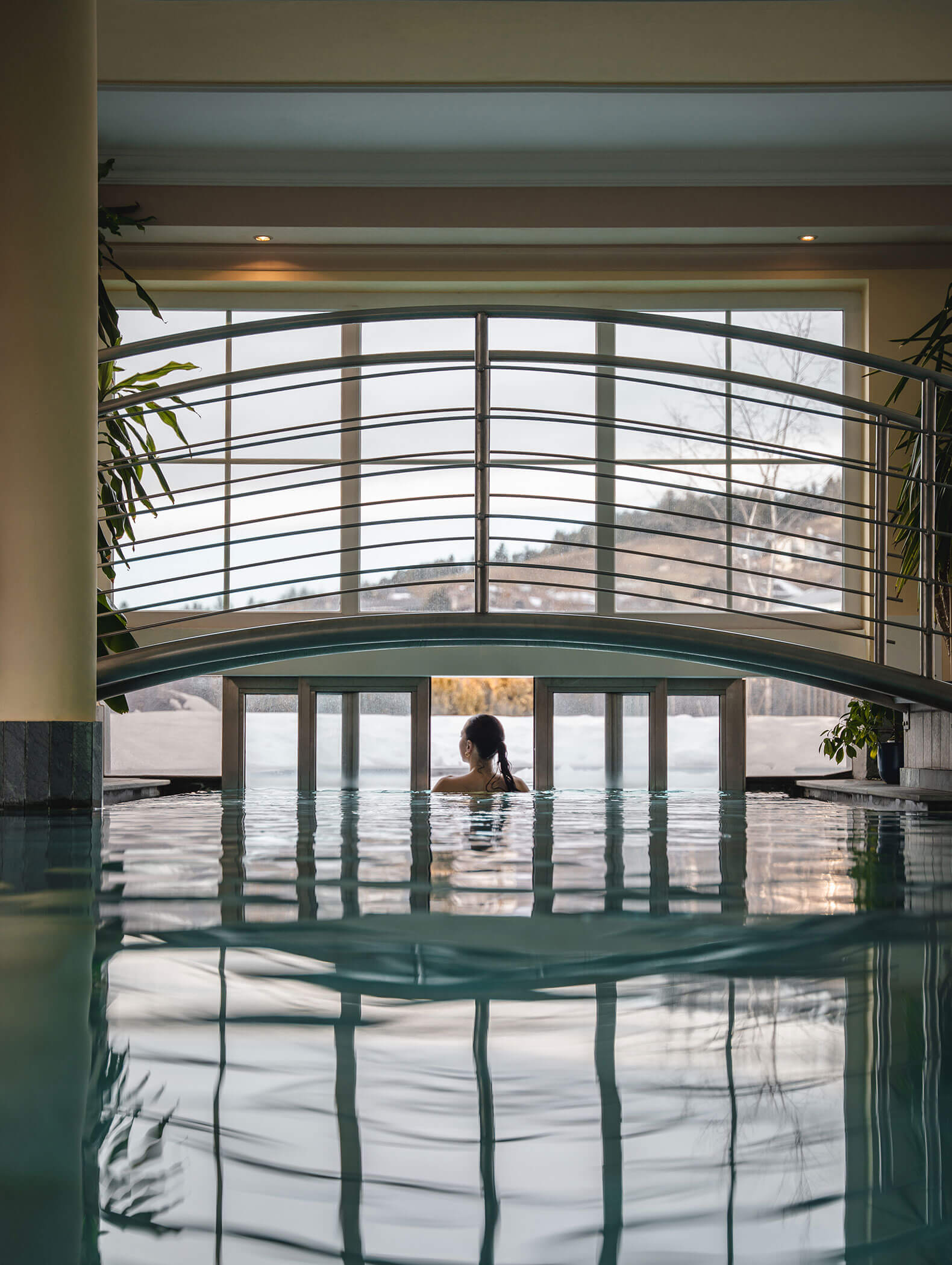 Eine Frau schwimmt durch eine Schiebetür vom Innenpool in den Außenpool - Vitalhotel Erica