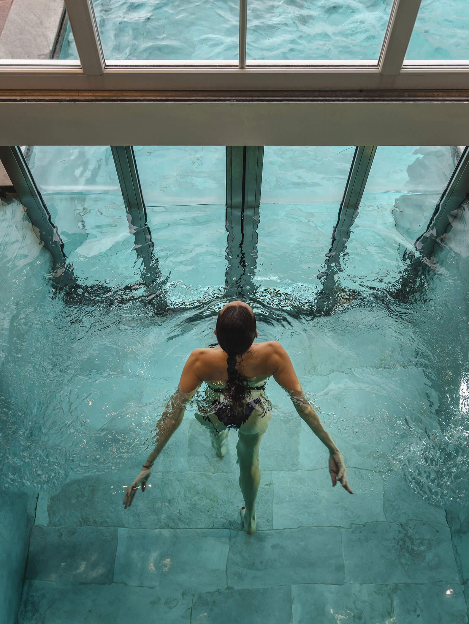 Vista dall'alto di una donna in piscina verso la porta scorrevole verso l'esterno - Vitalhotel Erica
