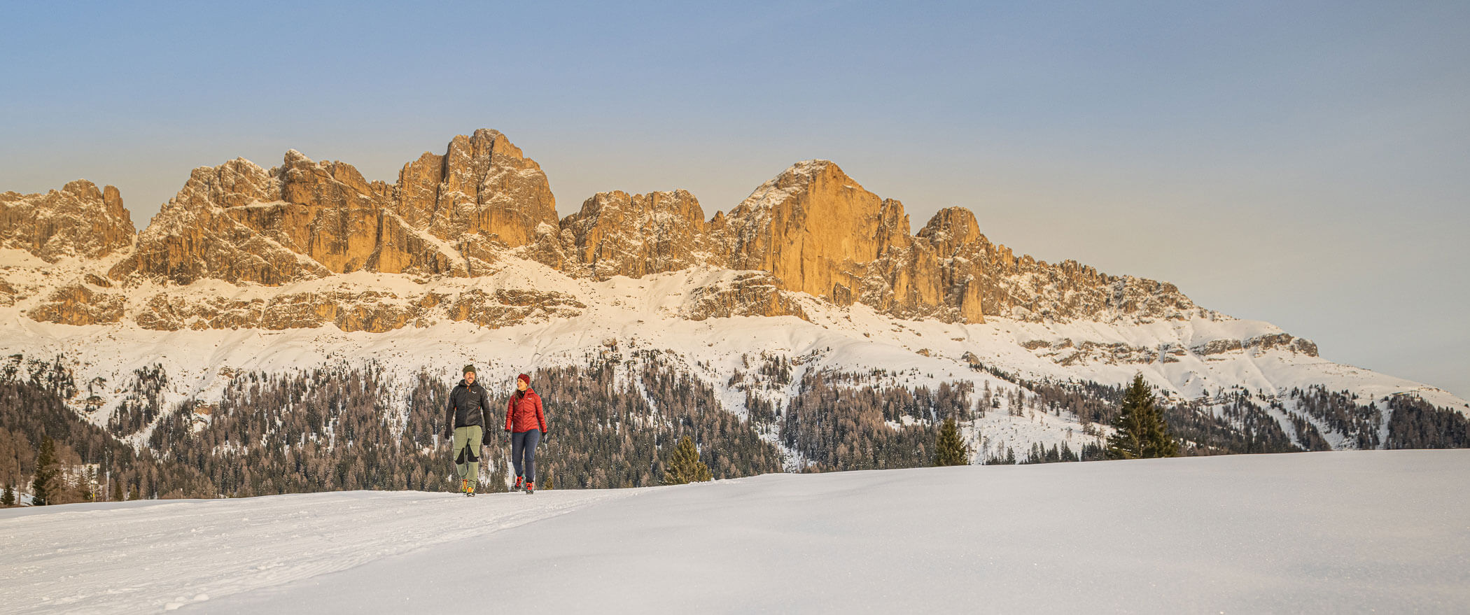 Due escursionisti su un sentiero innevato, con alle spalle lo sfondo delle Dolomiti - Vitalhotel Erica