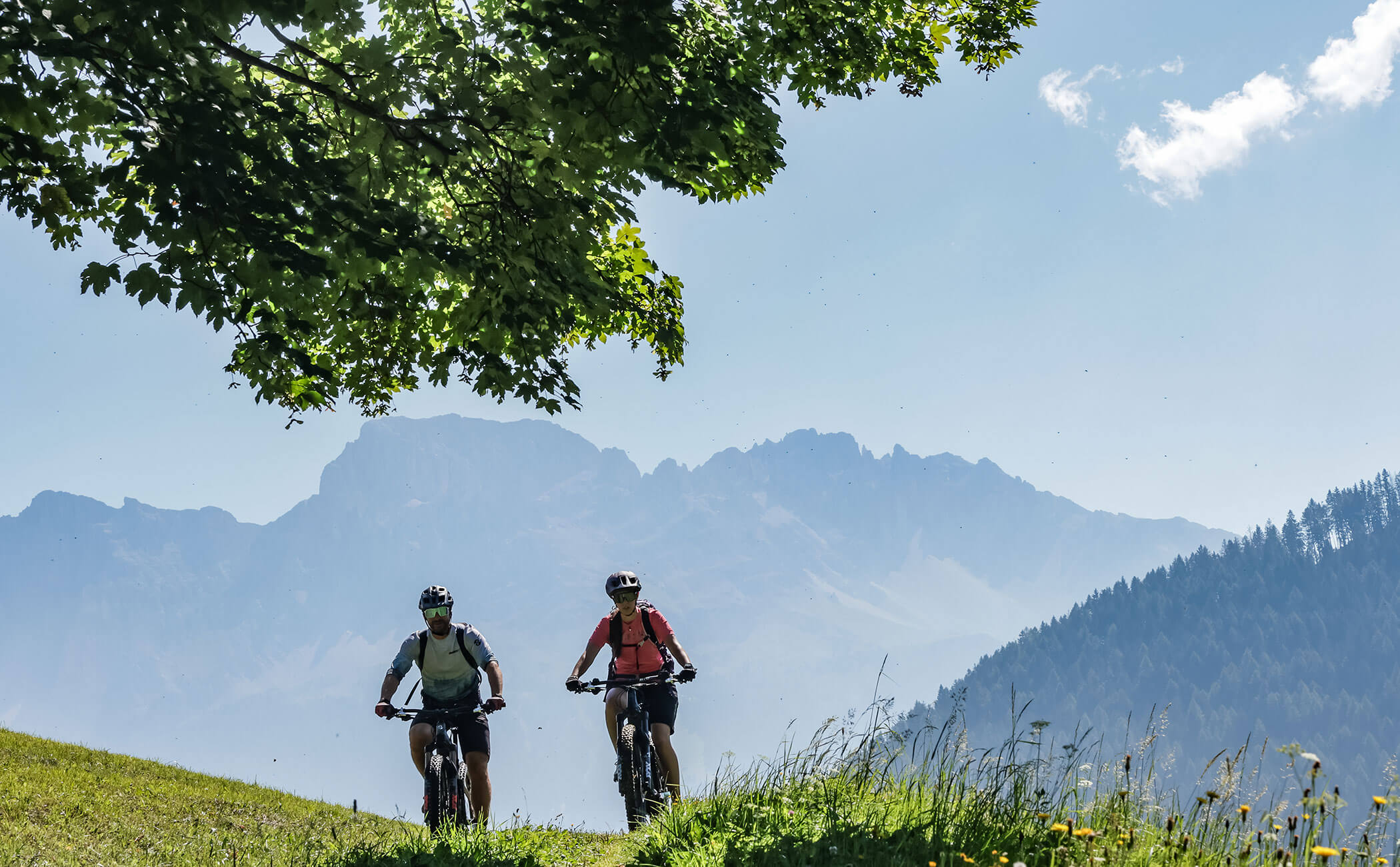 Ein Paar fährt mit den Mountainbikes über einen grünen Feldweg in den Bergen - Vitalhotel Erica