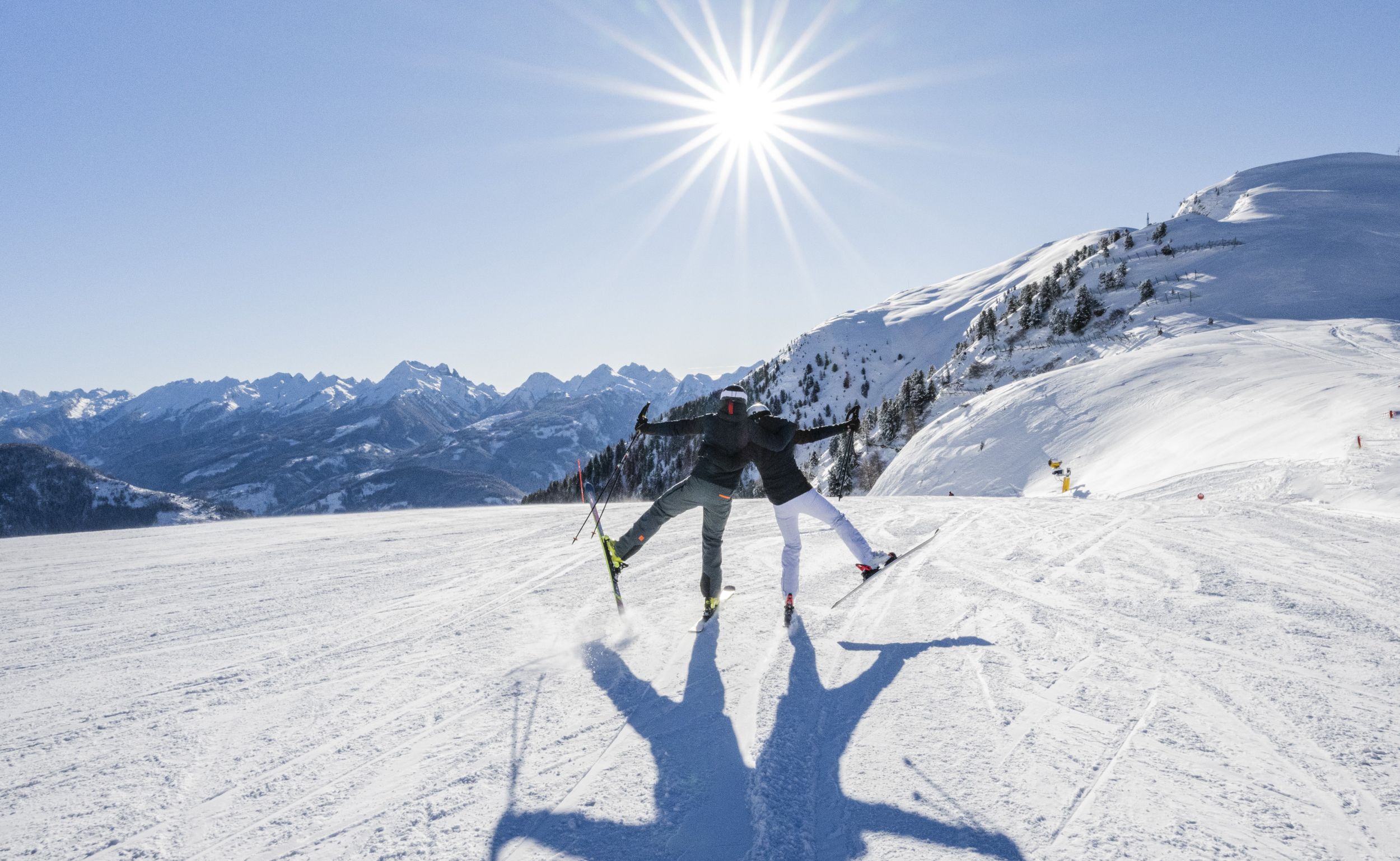 Zwei Skifahrer auf einem Berghang, die mit ausgestreckten Armen der strahlenden Sonne entgegenblicken. - Vitalhotel Erica